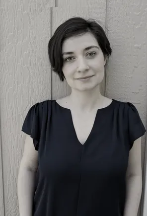 Alina Bochkacheva, smiling, in a black top against a wooden wall